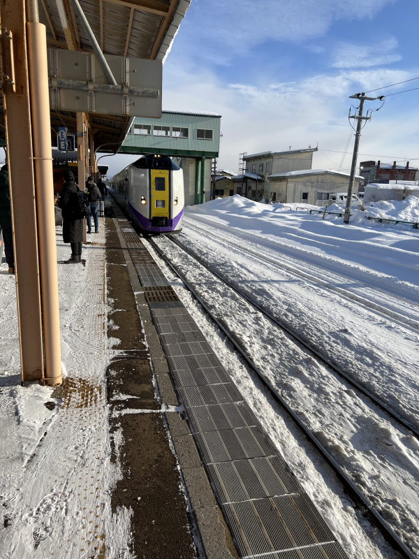 Snowy train platform with a train visible. Sun is shining